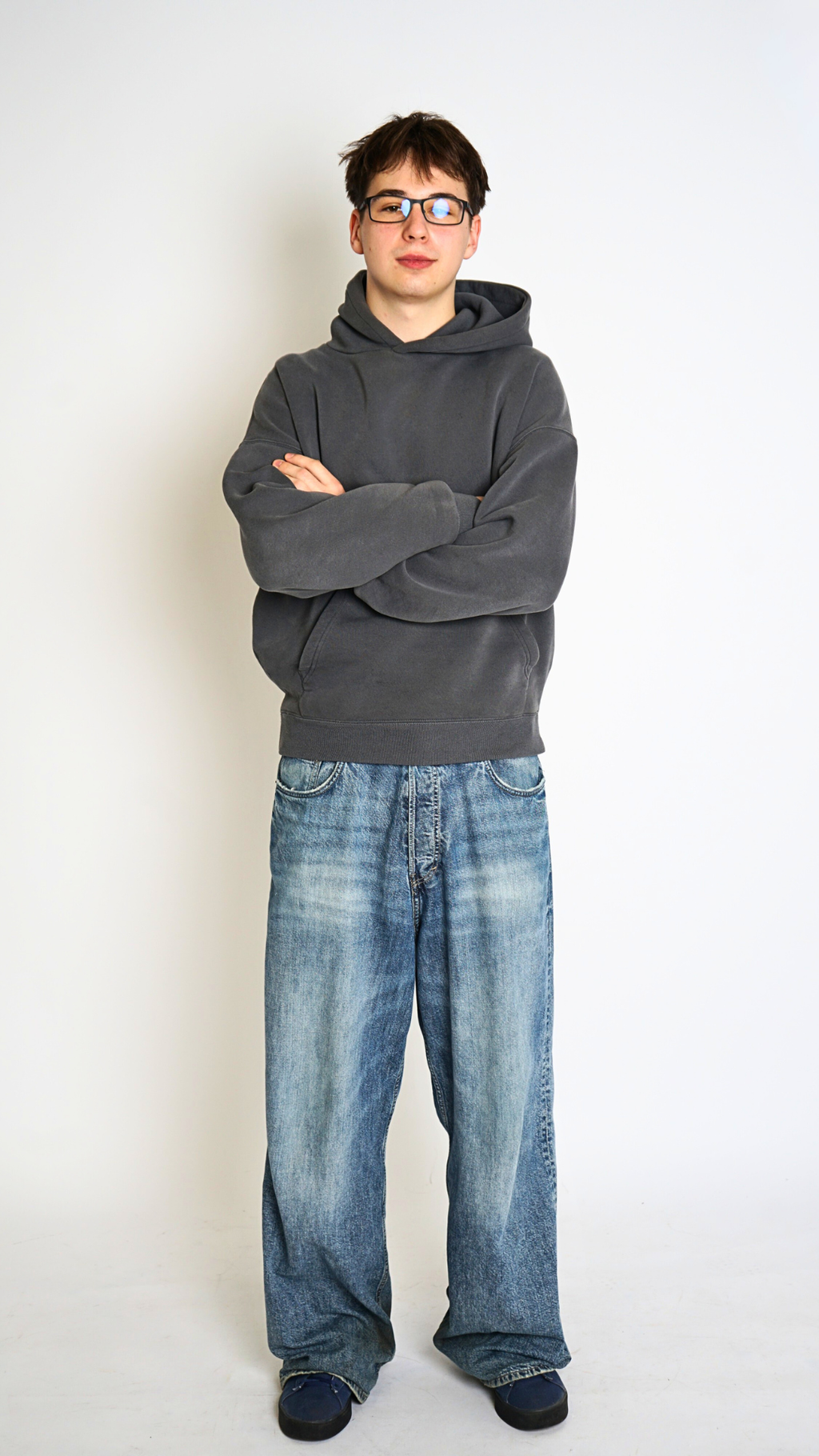 Person wearing a gray hoodie and blue jeans standing against a white background