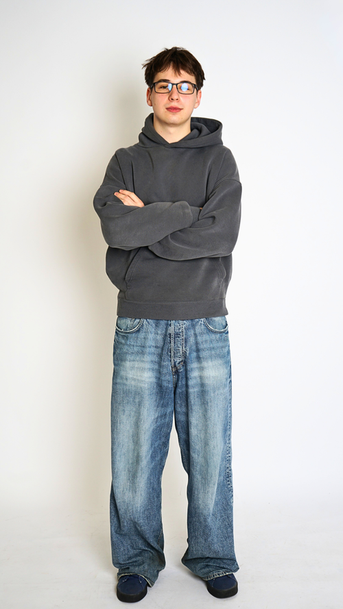 Person wearing a gray hoodie and blue jeans standing against a white background
