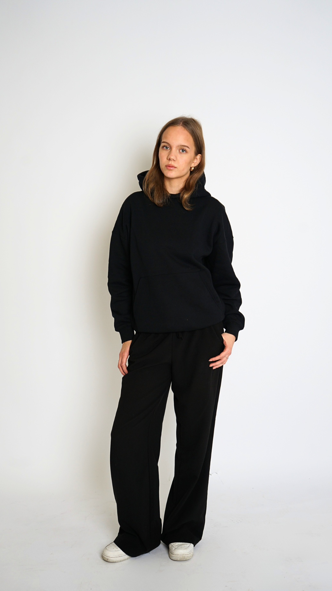 Person wearing a black hoodie and black pants on a white background