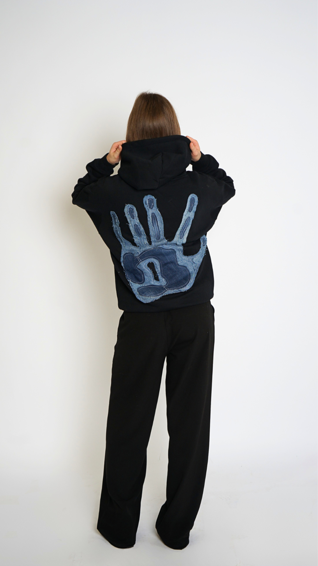 Person wearing a black hoodie with a blue handprint design on the back, standing against a white background.