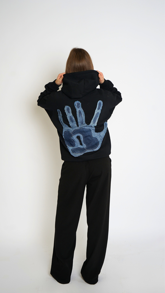 Person wearing a black hoodie with a blue handprint design on the back, standing against a white background.