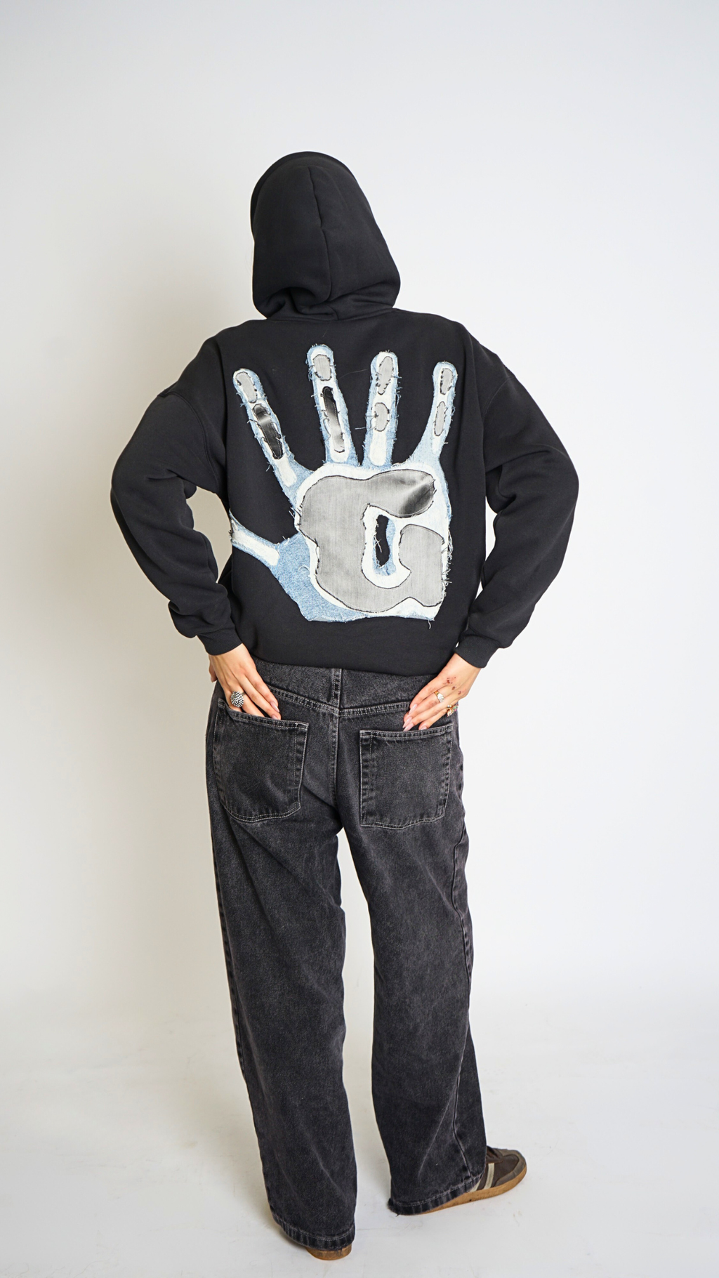 Person wearing a black hoodie with a handprint design on the back against a white background