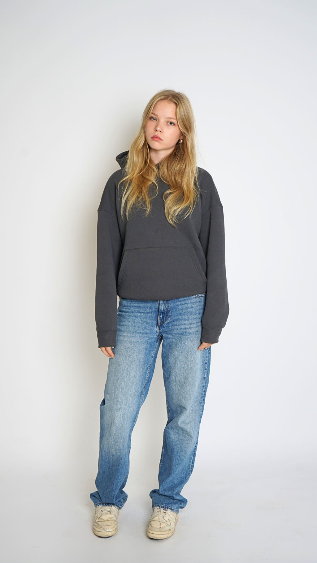 Woman wearing a dark gray hoodie and blue jeans against a white background