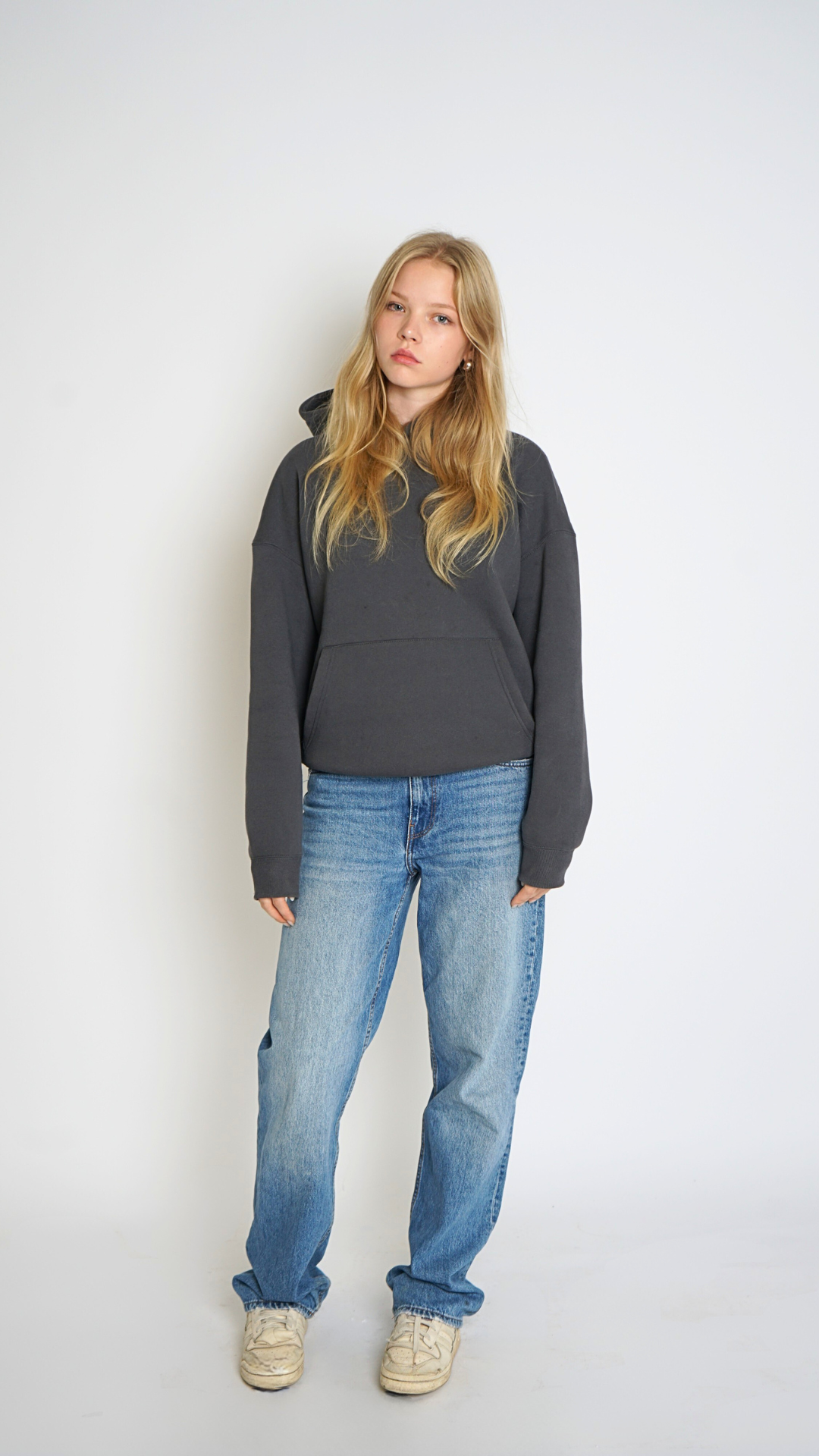 Woman wearing a dark gray hoodie and blue jeans against a white background
