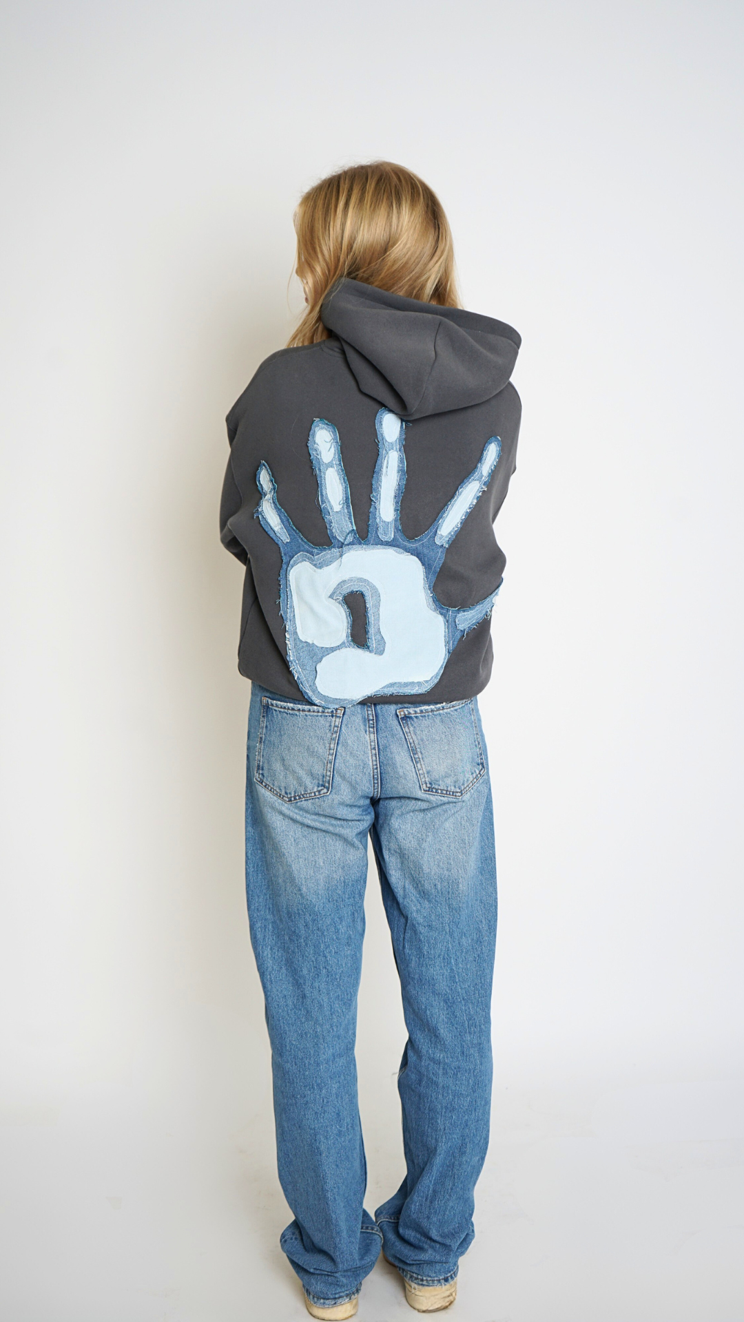 Person wearing a hoodie with a handprint design on the back, standing against a plain background.