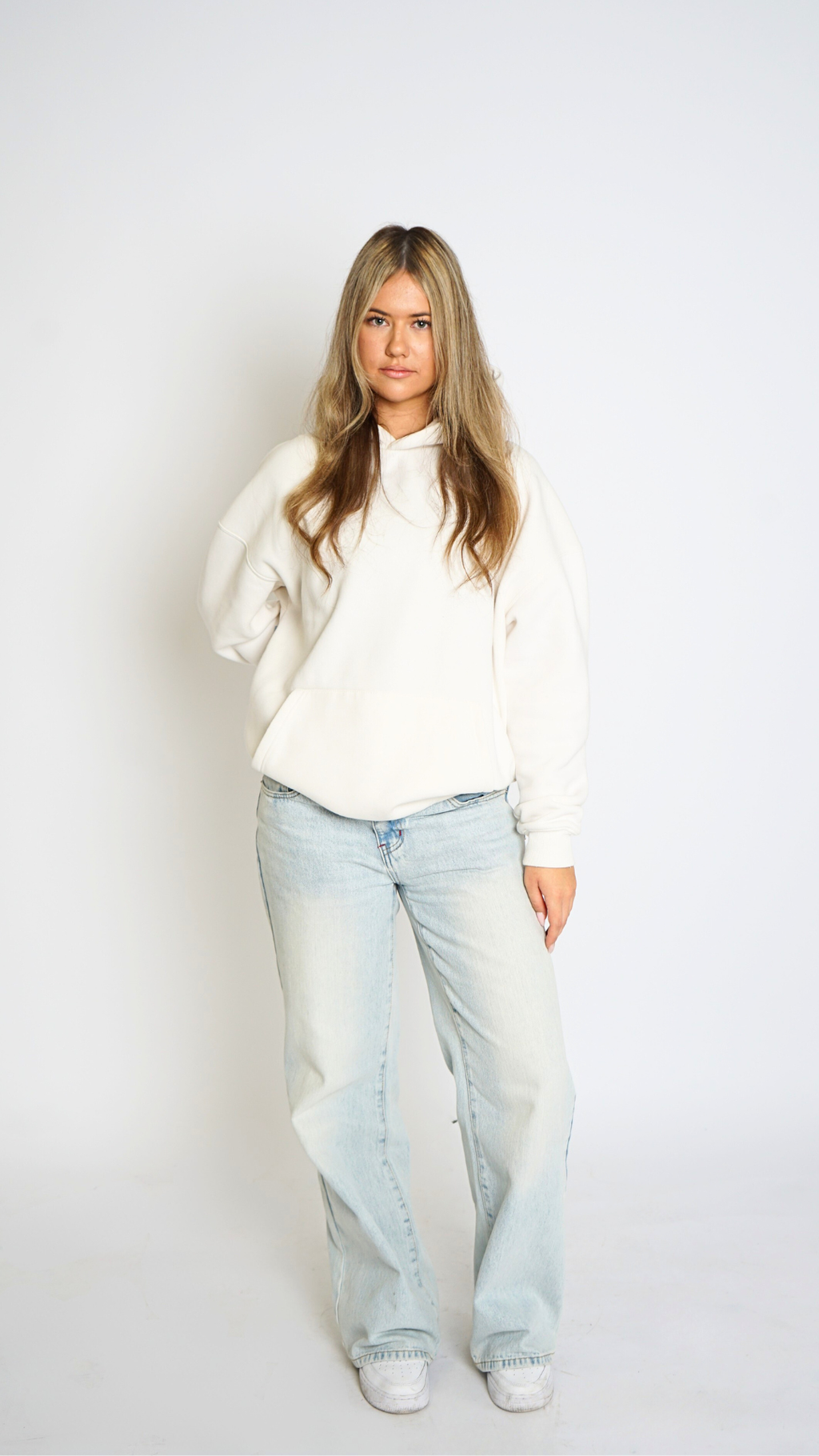 Woman wearing a white sweater and light blue jeans against a plain background