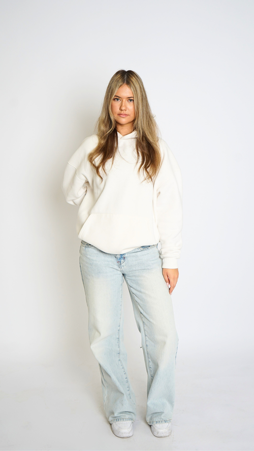Woman wearing a white sweater and light blue jeans against a plain background