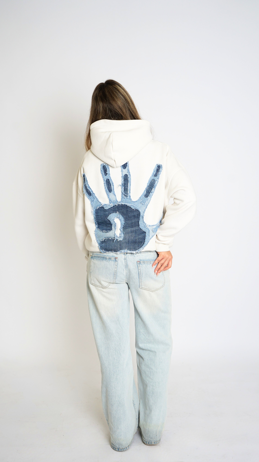 Person wearing a white hoodie with a blue handprint design on the back, standing against a plain background.