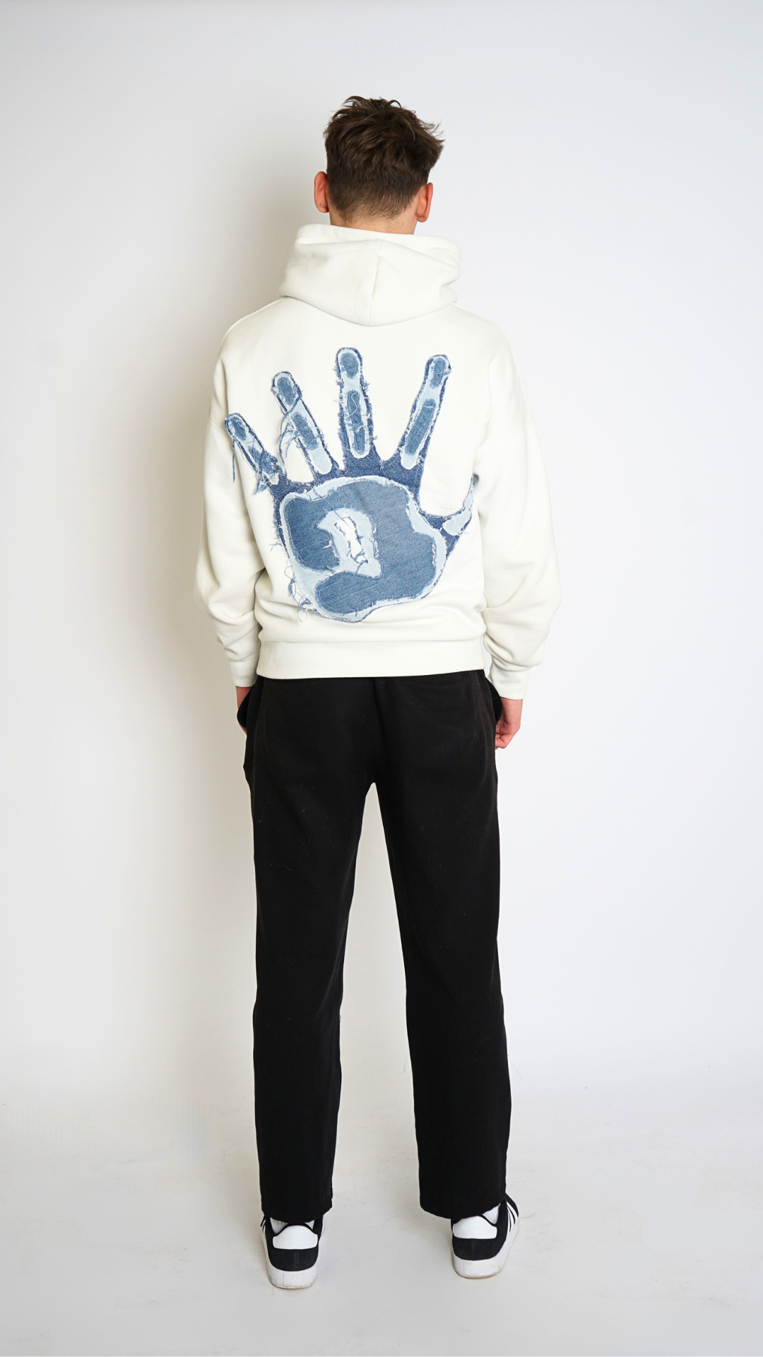 Person wearing a white hoodie with blue handprints on the back against a white background